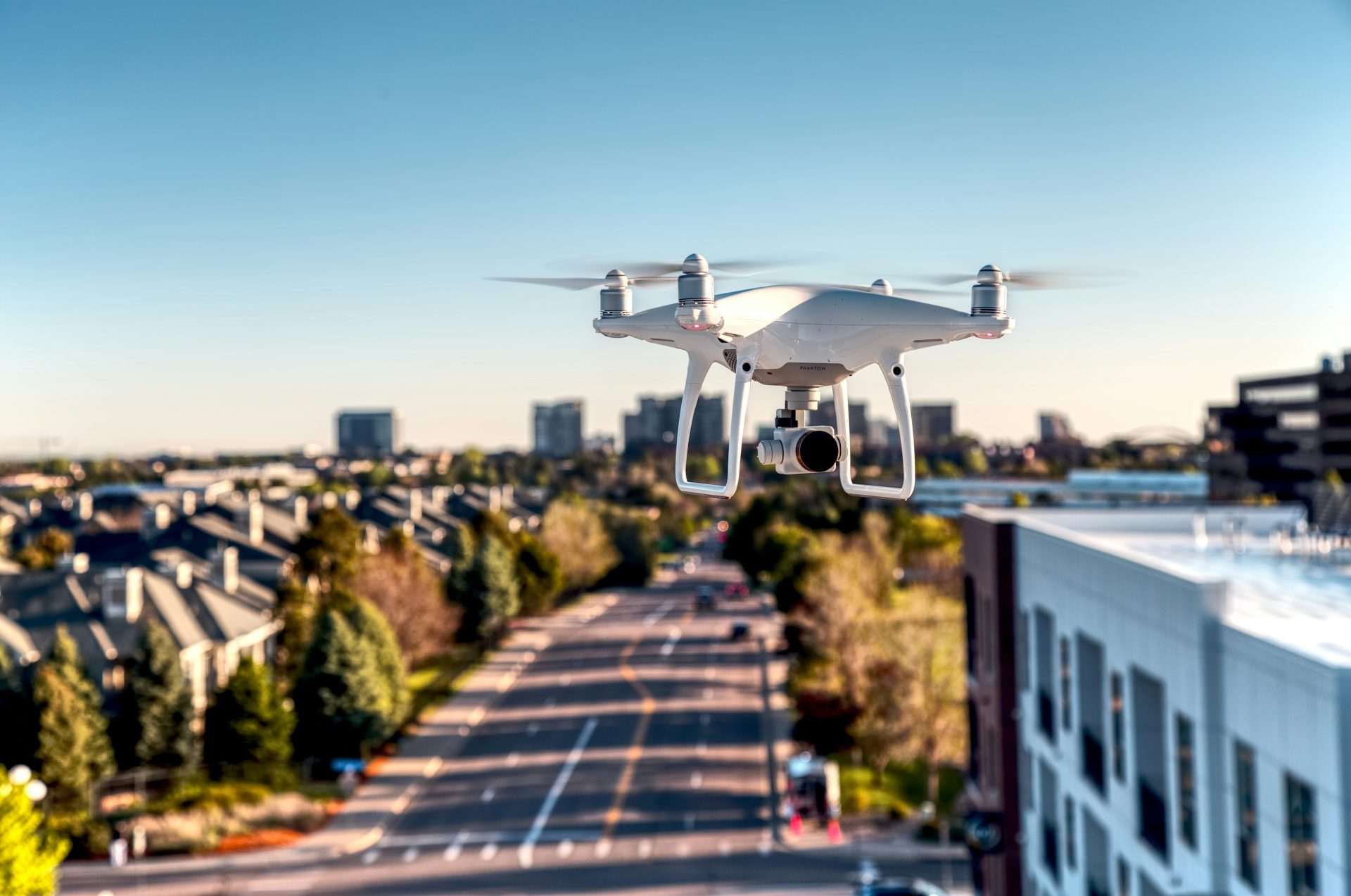 Weiße Drohne fliegt tagsüber über die Stadt.